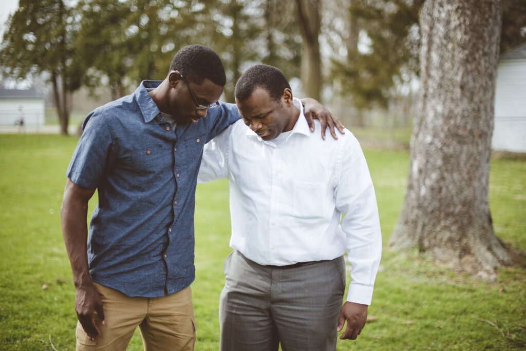 African-American male friends standing with their hands on the shoulders and praying