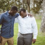 African-American male friends standing with their hands on the shoulders and praying