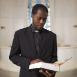 Black Young Man as Priest Holding Bible at Church Altar