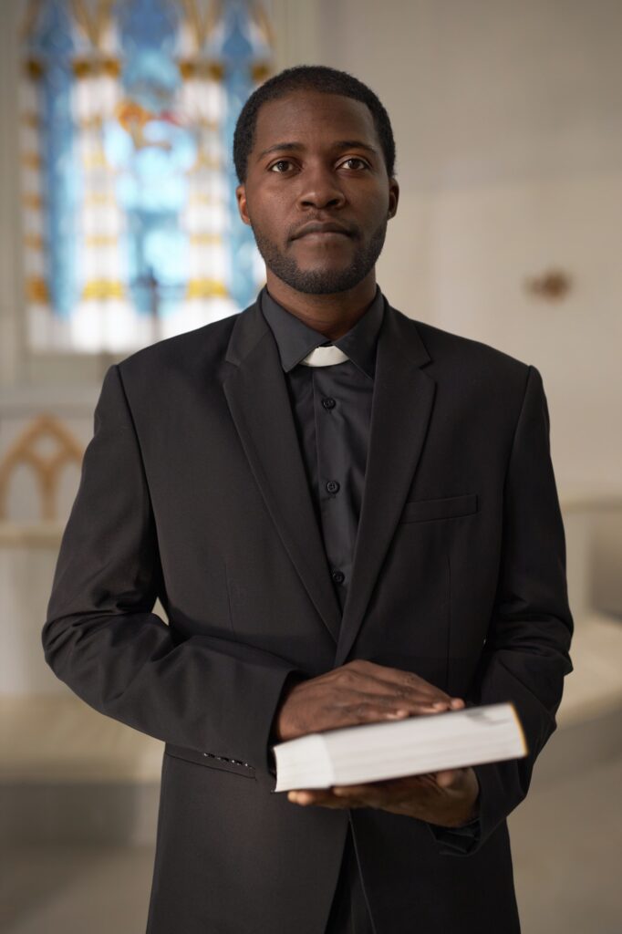 Black Young Man as Priest Holding Bible Standing at Altar in Church