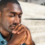 Close up young black man with eyes closed praying outside