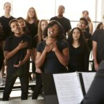 Male And Female Students Singing In Choir With Teacher At Performing Arts School