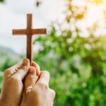 man praying with cross in nature sunrise background, Symbol of Faith.