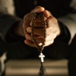 Priest Holding Wooden Rosary and Praying in Sunlight