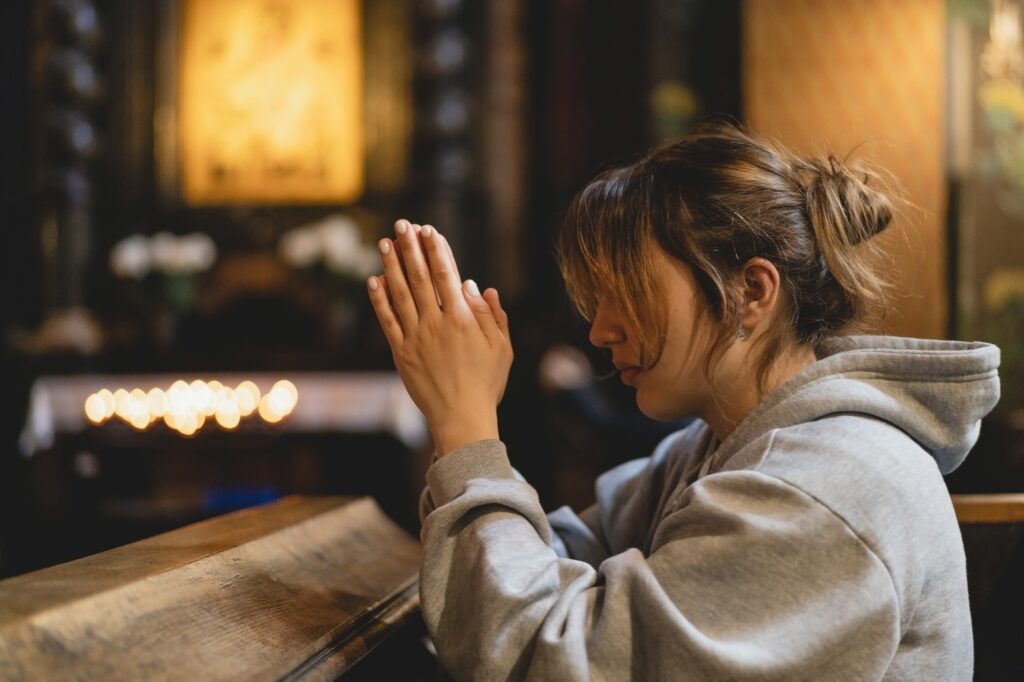 Woman praying on her knees in an ancient Catholic temple to God.