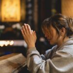 Woman praying on her knees in an ancient Catholic temple to God.