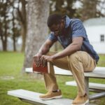 Young African-American male sitting with closed eyes with the Bible in his hands